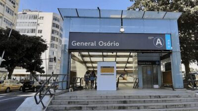 Entrada da estação General Osório do metrô do Rio de Janeiro, com pedestres e táxis ao fundo, em dia ensolarado.
