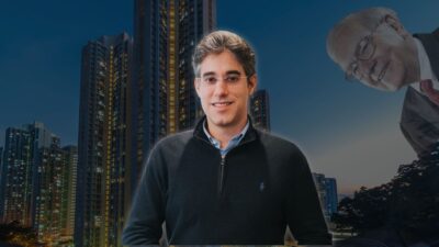 César Paiva, gestor da Real Investor, em frente a prédios residenciais, com referência a Warren Buffett ao fundo, simbolizando a filosofia de investimentos da gestora.