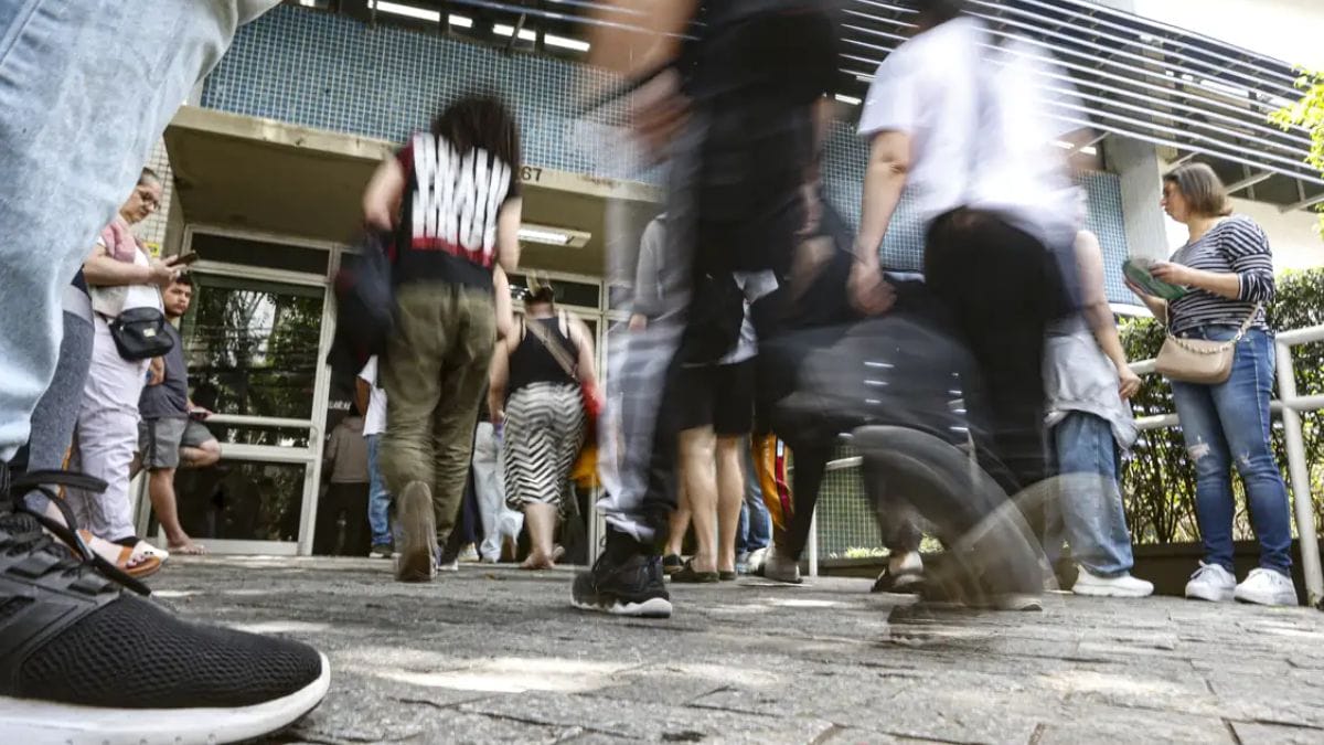 Candidatos chegam e se movimentam em frente a um prédio escolar antes da abertura dos portões para a aplicação das provas do CONCURSO PÚBLICO NACIONAL UNIFICADO (CNU 2025). Pessoas aparecem em pé e caminhando, algumas com mochilas e materiais na mão, em clima de expectativa no dia do exame