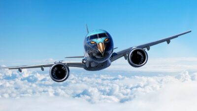 Avião Embraer E195-E2 personalizado com pintura de águia no nariz da aeronave, voando acima das nuvens sob um céu azul claro
