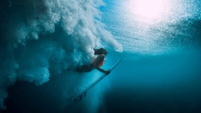 Surfista com prancha está mergulhada e passando debaixo de uma onda, no mar
