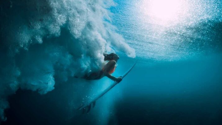 Surfista com prancha está mergulhada e passando debaixo de uma onda, no mar