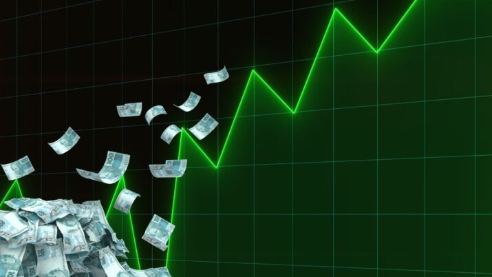 Gráfico verde de alta diante de um monte de notas de cem reais