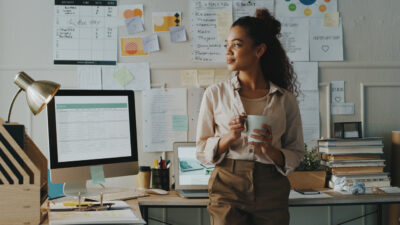 Shot of an attractive young businesswoman standing and looking contemplative while holding a cup of coffee in her home office