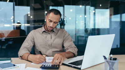 A young African American male auditor, banker working in office at desk with laptop and documents