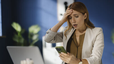 Shocked businesswoman reading a text message on cell phone in the office.