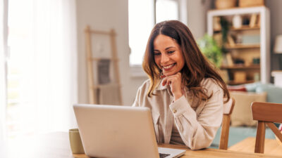 Young woman working from home and smiling at laptop