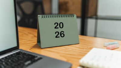 Cropped shot of laptop, table calendar for new year, notebook and coloured markers on office desk