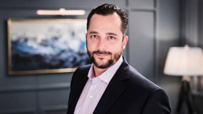 Foto do CIO do EFG Private Wealth Management, Luis Ferreira, em uma sala com uma quadro ao fundo. Ele usa terno azul escuro e camisa rosa claro.