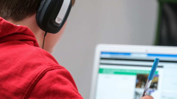 Jovem olhando para a tela de um notebook e usando fones de ouvido