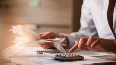 Close up of businesswoman using calculator while going through financial bills.