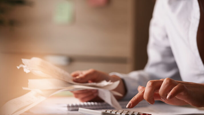 Close up of businesswoman using calculator while going through financial bills.