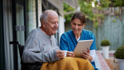 Friendly nurse and senior man on wheelchair using digital tablet