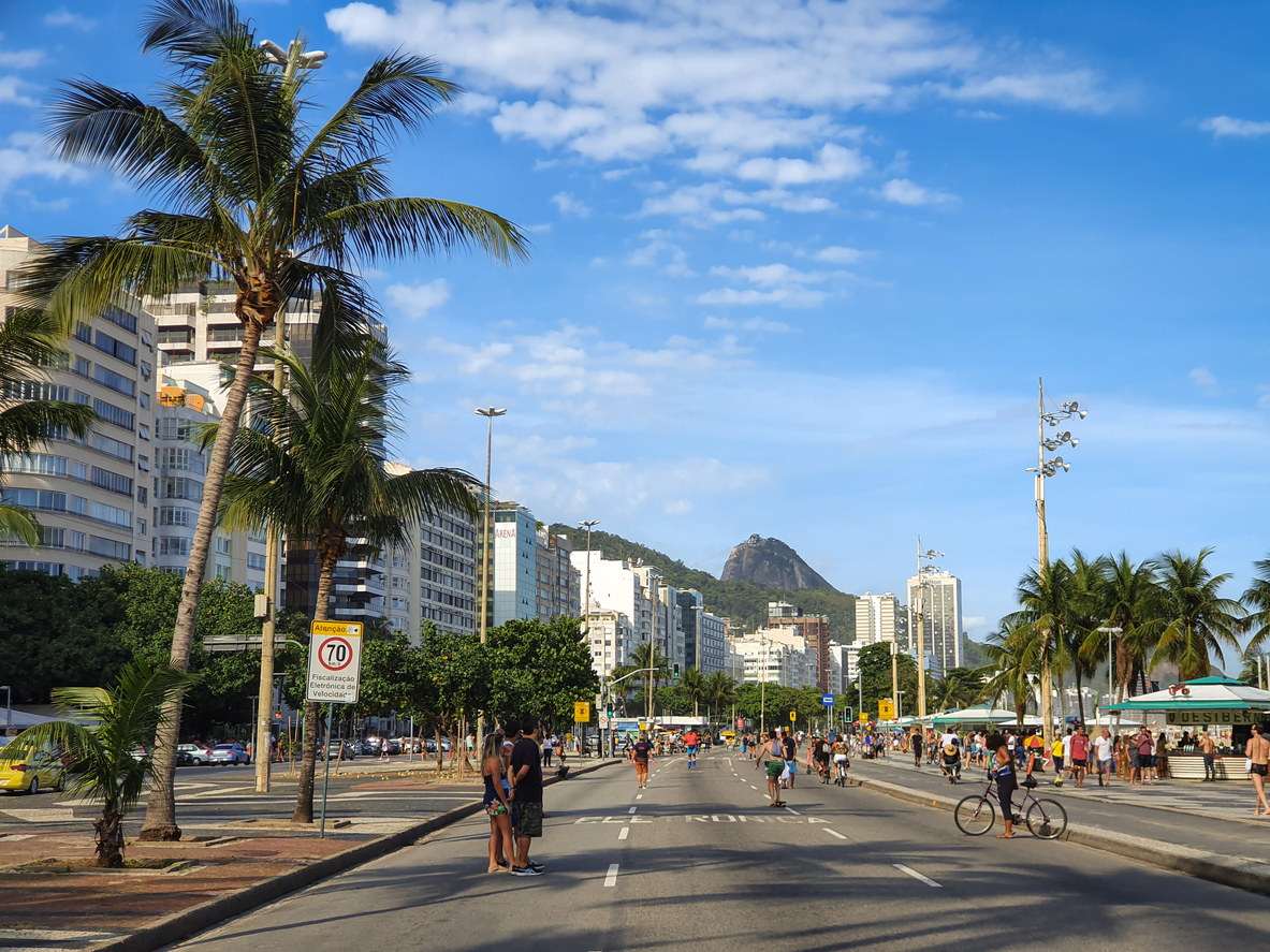 Rio de janeiro, Brazil - December 8, 2019: Avenida Atlântica in Copacabana, Rio de Janeiro, Brazil, is seen bustling with people walking, cycling, and enjoying the open street during a sunny day. The iconic beachfront avenue is flanked by tall buildings on one side and palm trees lining the promenade. 