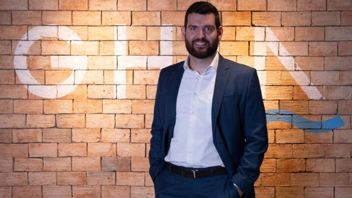Em um fundo de parede de tijolos, Bruno de Paula, diretor da Ghia Multi Family Office, aparece de terno azul, camisa branca e mãos nos bolsos