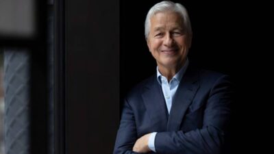 Foto em fundo escuro de Jamie Dimon, CEO do JP Morgan. Ele usa terno azul e está de braços cruzados