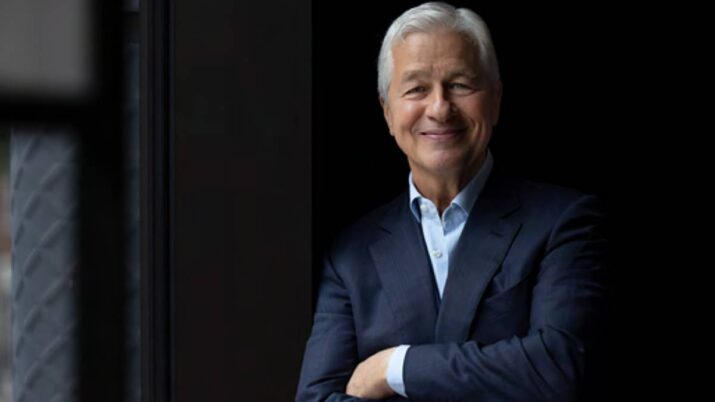 Foto em fundo escuro de Jamie Dimon, CEO do JP Morgan. Ele usa terno azul e está de braços cruzados