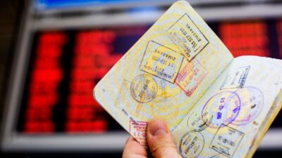 Passport with custom entry stamps in-front of information board at airport