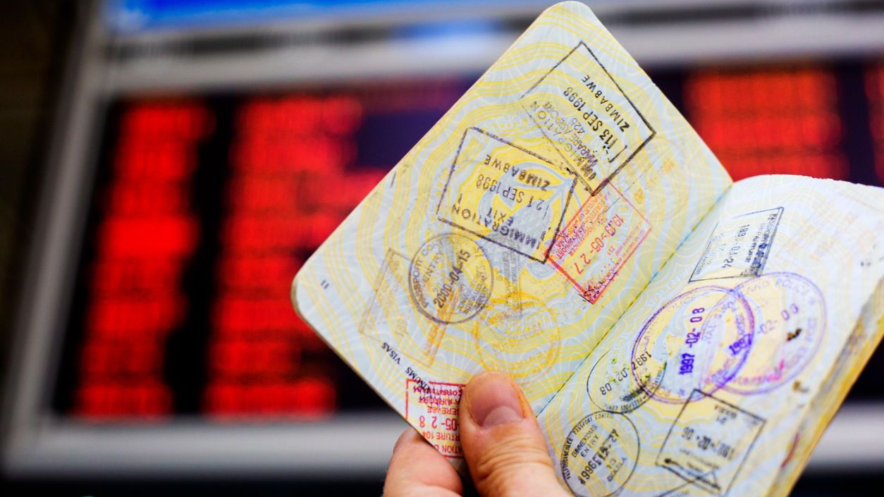 Passport with custom entry stamps in-front of information board at airport
