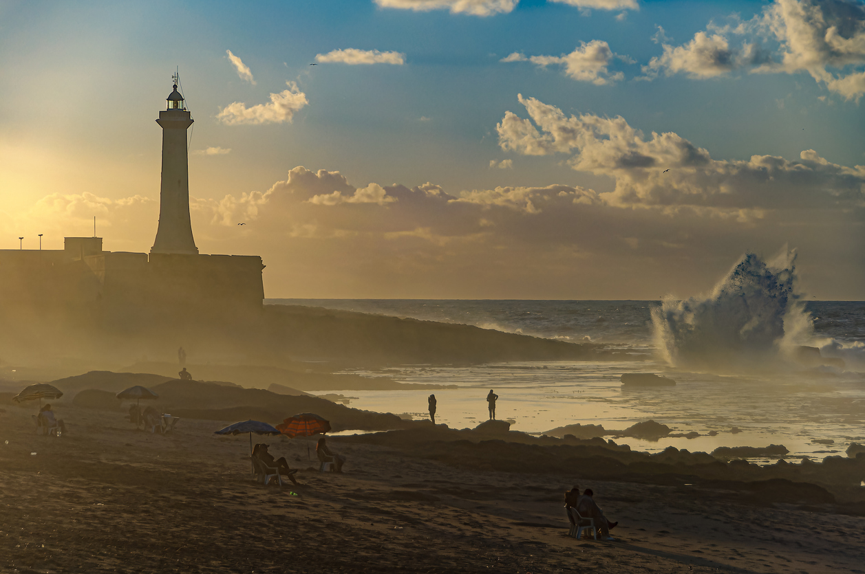 Marrocos. Rabat. As pessoas relaxam na praia ao pôr do sol em frente ao mar agitado
