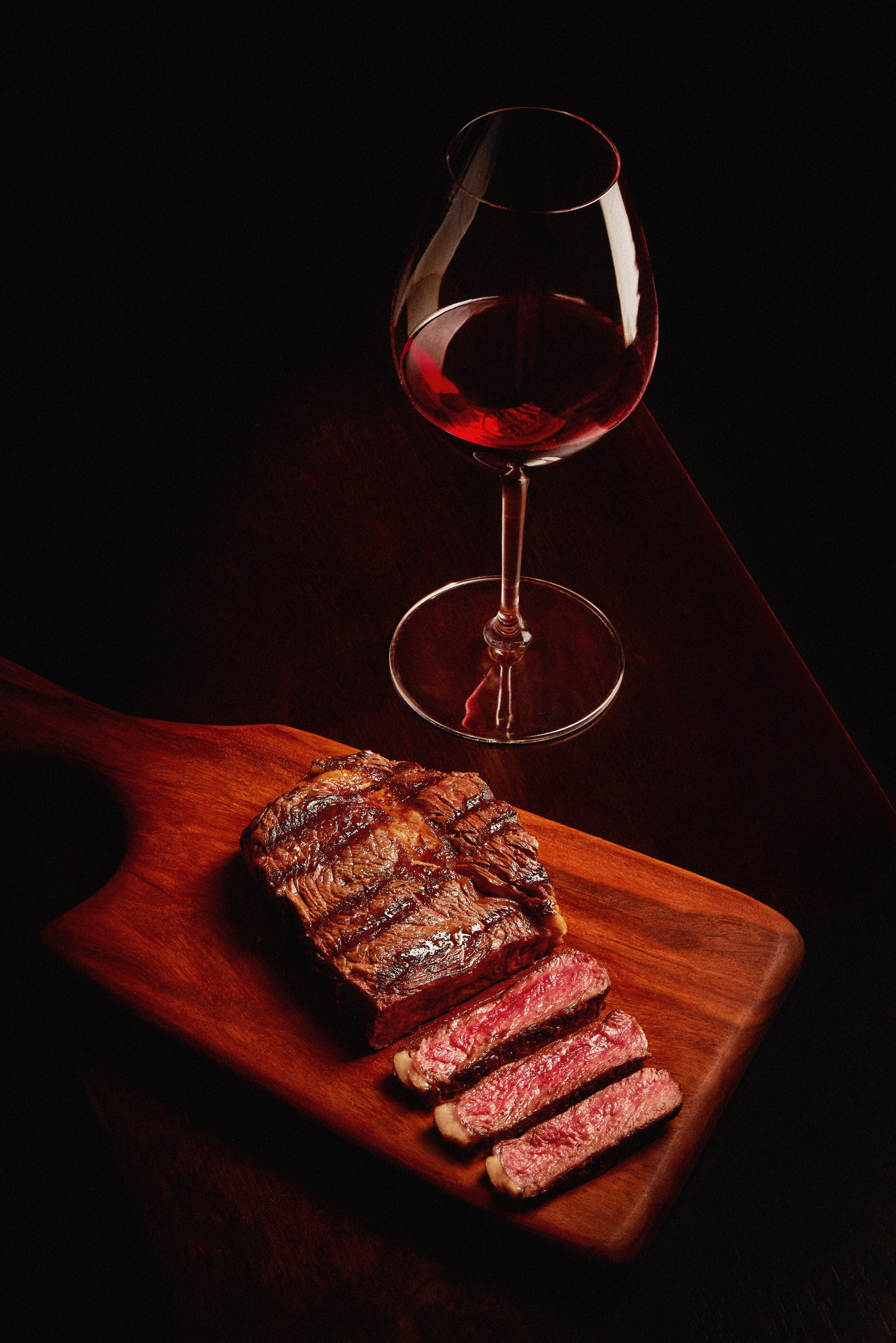 Bife ancho fatiado sobre tábua de madeira acompanhado de uma taça de vinho