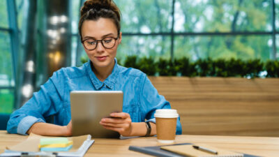 Nice-looking young caucasian businesswoman using tablet at the desk in modern office