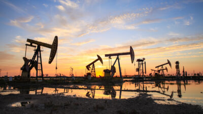 Oil field site, in the evening, oil pumps are running, The oil pump and the beautiful sunset reflected in the water
