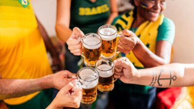 Close de torcedores brasileiros brindando com cerveja com camiseta do brasil