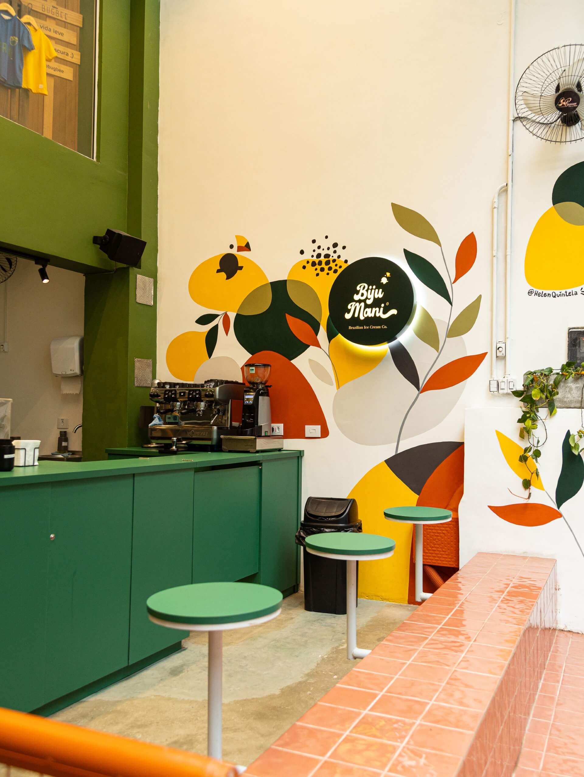 sorveteria com bancada e cadeiras verdes e parede colorida (amarelo, vermelho e verde)