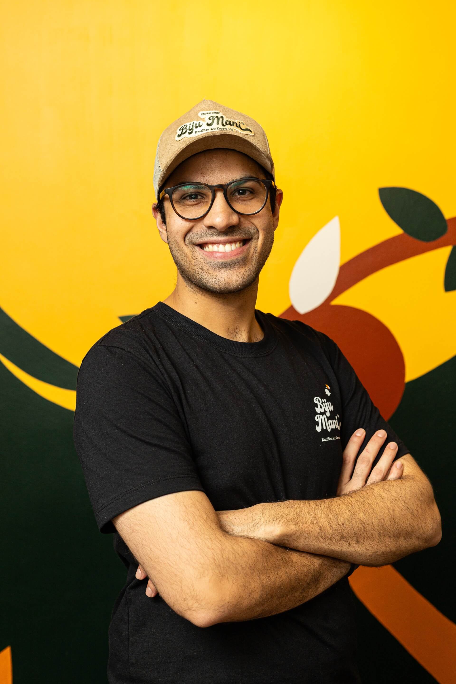 Guilherme frente à parede colorida de braços cruzados 
