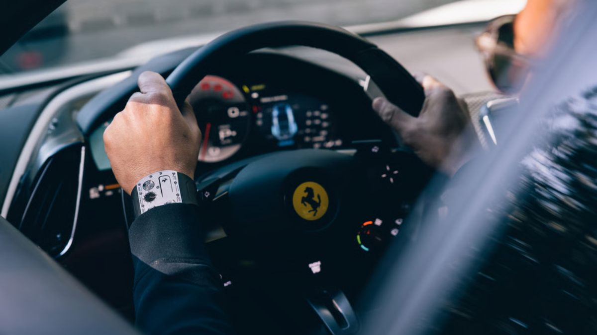 pessoa dirigindo ferrari com mão no volante e relógio no pulso da RM