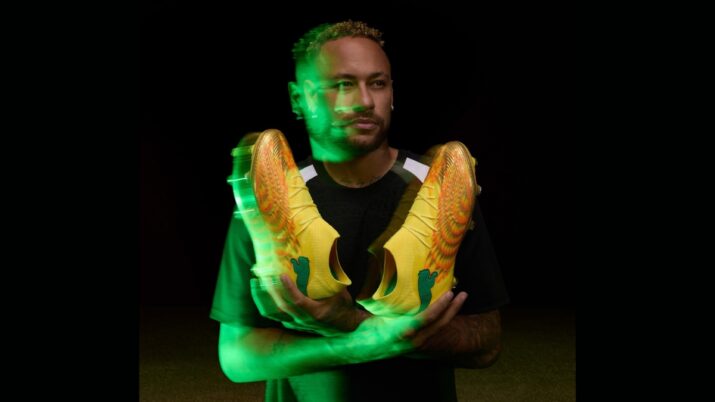 Neymar em fundo preto segurando nas mãos par de chuteiras amarelas