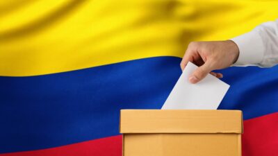 ID da foto:2232370416 Eleição na Colômbia. Mão do homem que põe seu voto na urna e na bandeira da Colômbia no fundo