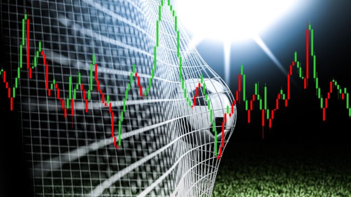 Imagem mostra uma bola de futebol entrando na rede de um gol, com gráficos de ações e mercado financeiro na frente