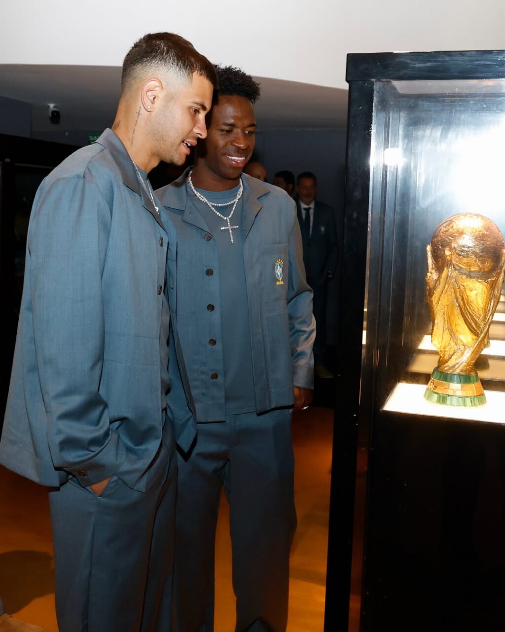 Bruno Guimarães e Vini Jr. no museu da CBF em frente a taça vestidos com ricardo almeida