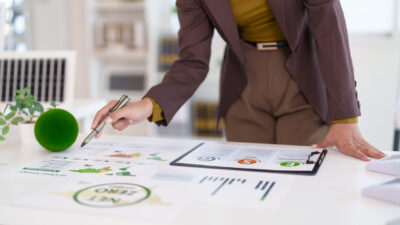 Adult professional hand pointing pen analyzing ESG sustainability business reports charts graphs office meeting future strategy net zero goals corporate responsibility