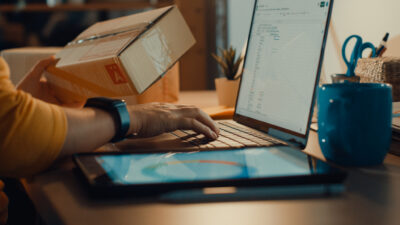 autônoma usando laptop para embalar caixas de papelão na sala de casa à noite. Trabalhando em casa.