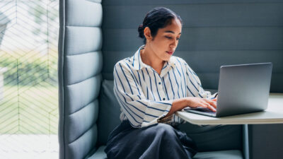 Focused Professional Woman Working on Laptop in a Modern Office Booth