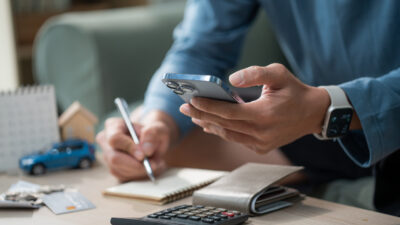 Man hand using smart phone and calculator to manage monthly expenses, saving for house and car, personal finance budget planning concept at home
