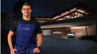 No primeiro plano, chef Alberto Landgraf aparece sorrindo e usando um avental azul com o logo BTG Pactual. Ao fundo, o Terminal BTG Pactual à noite.