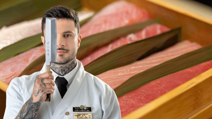 Chef Allan Beckmann aparece com um cutelo cobrindo metade de seu rosto. Ao fundo, uma caixa com cortes de peixe cru.