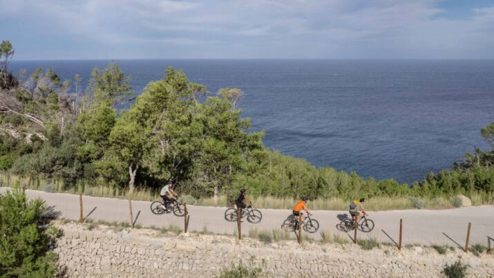 quatro pessoas andando de bike em um terreno elevado com vista para o mar