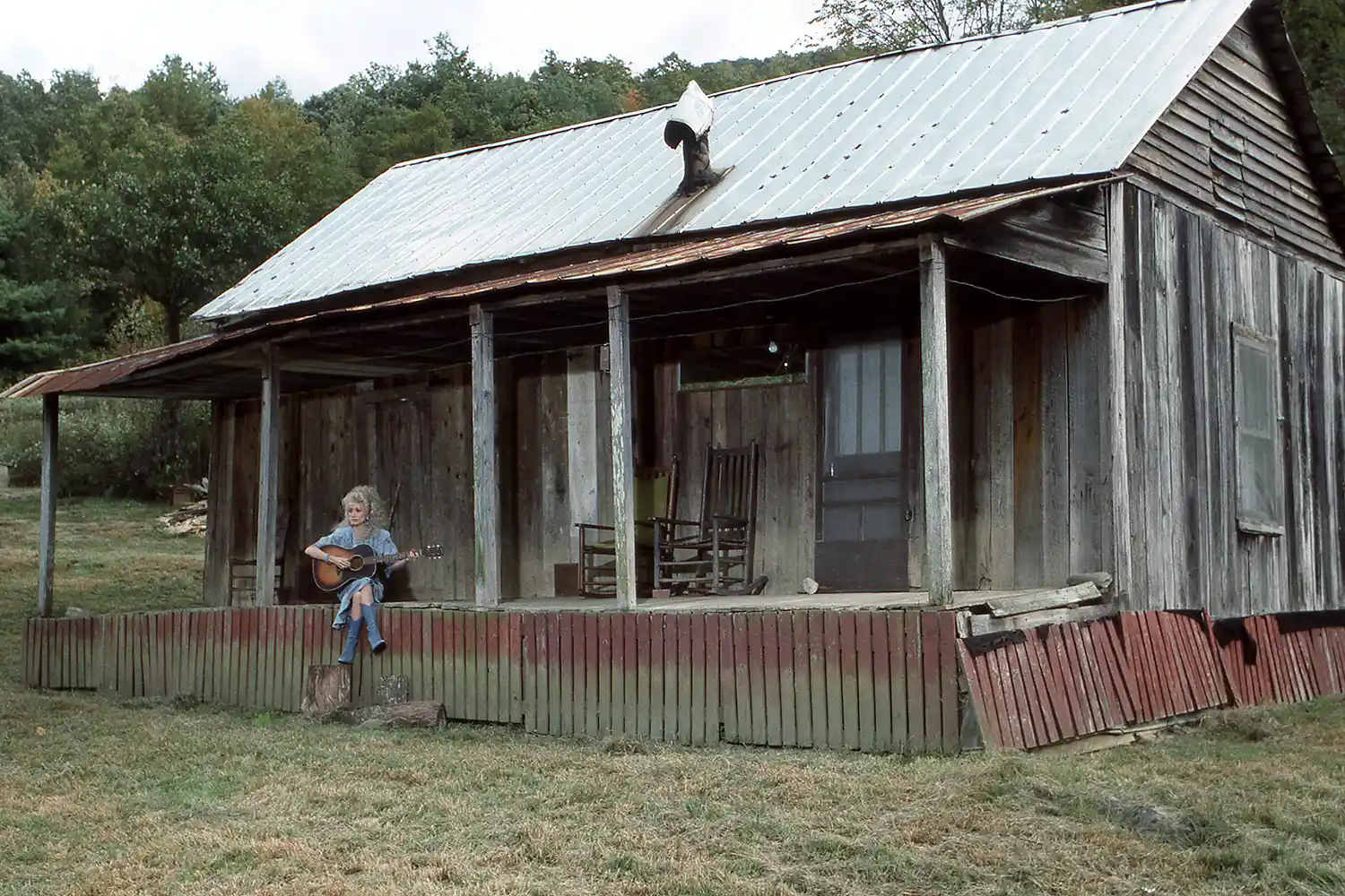 Dolly Parton sentada na réplica de sua casa de infância em Dollywood, em 1987