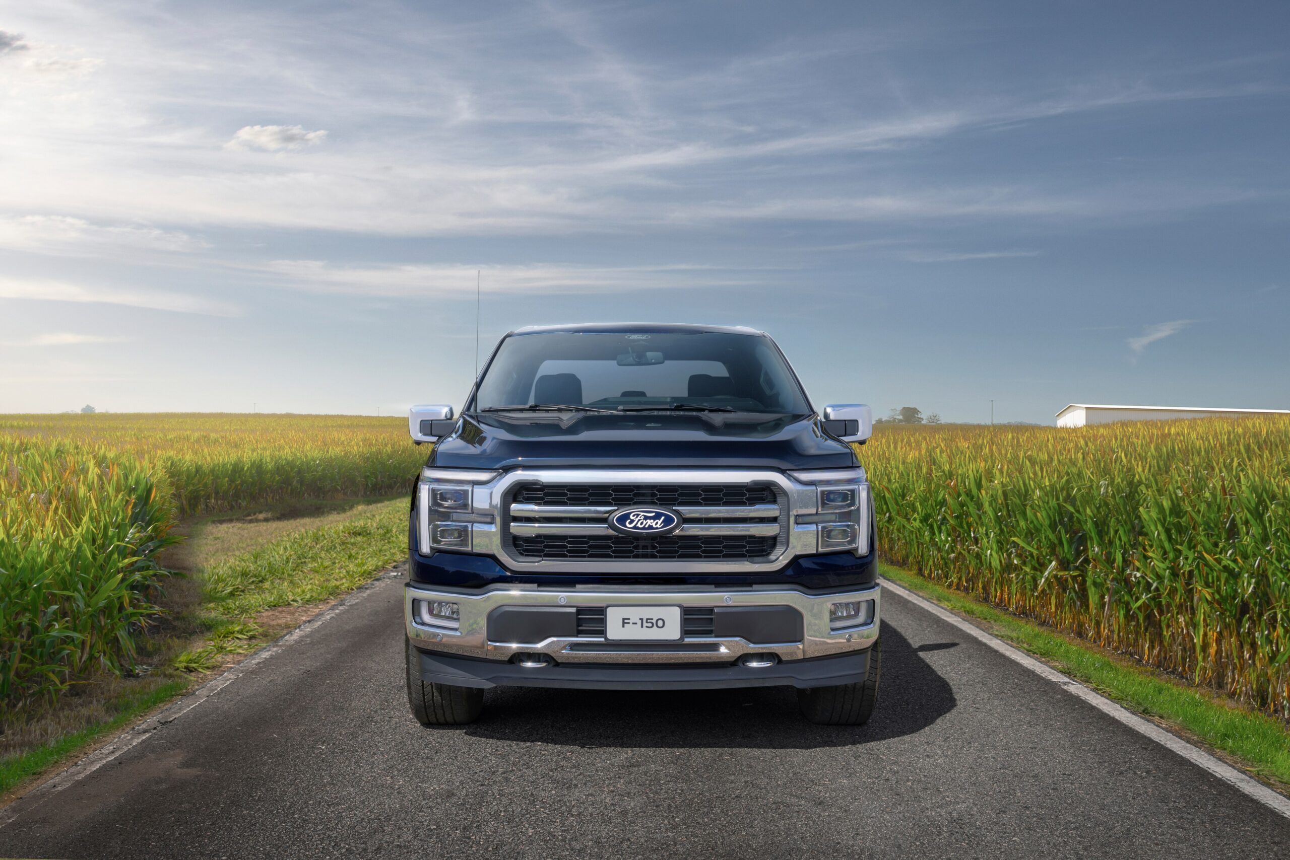 Ford F-150 Lariat preta vista de frente em uma estrada, ladeada por vegetação sob um céu azul anuveado