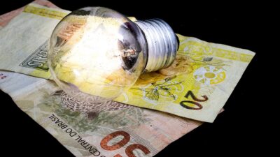 Notas de 20 e 50 reais sobre uma mesa preta e uma lâmpada em cima