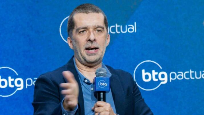 Mat Velloso Homem participa de painel no BTG Pactual Macro Day 2026, sentado em uma cadeira e falando ao microfone, diante de painel azul com a marca do banco.