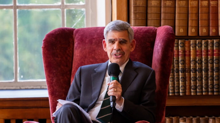 O economista Mohamed El-Erian está sentado em uma poltrona vermelha, segurando um microfone. Atrás dele, uma estante de livros.