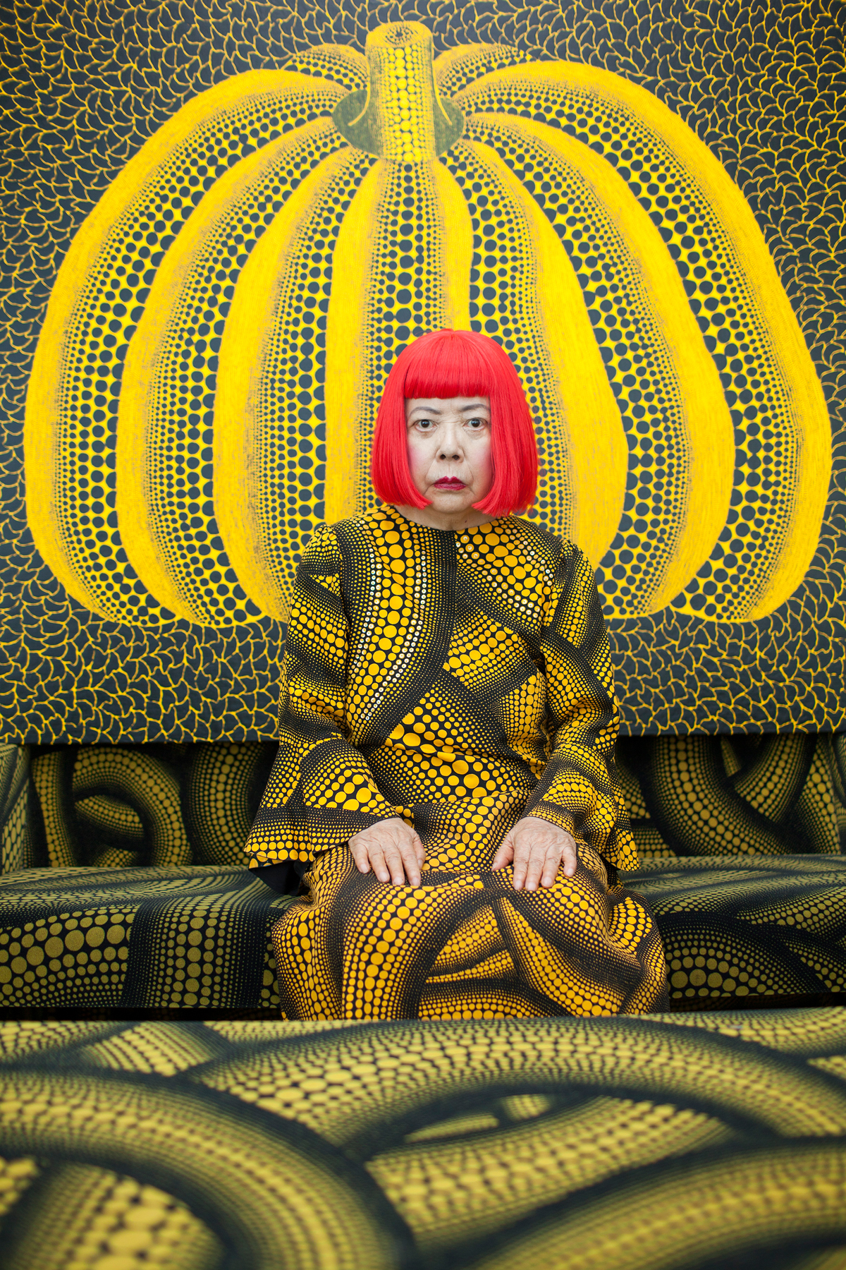 Yayoi Kusama sentada em frente sua obra Pumpkin