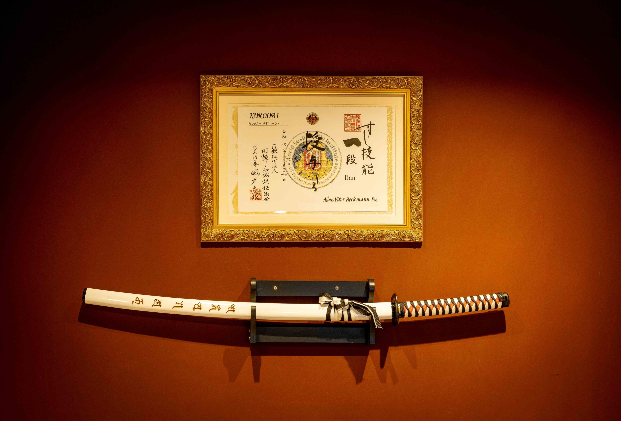 Parede terracota do Satori Omakase: acima, a certificação Kuro Obi; abaixo. uma katana (espada japonesa)