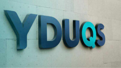 Logotipo da Yduqs em tons de azul, em uma parede clara
